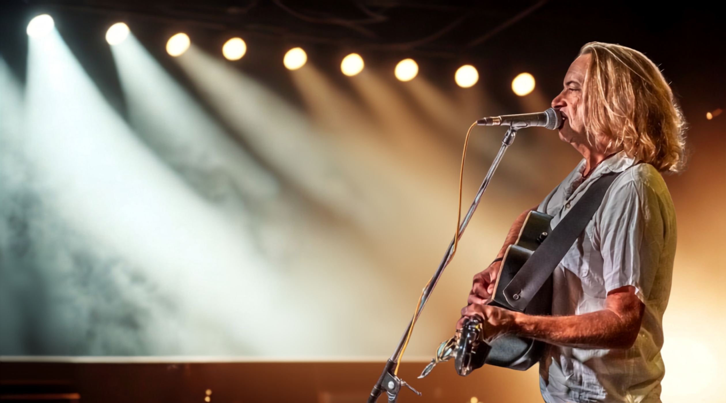 Brian Cristopher singing and playing guitar on stage under warm lights